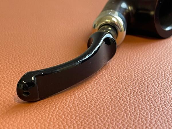 Gebogenes, dunkles Mundstück einer Pfeife auf orangenen, ledrigem Untergrund